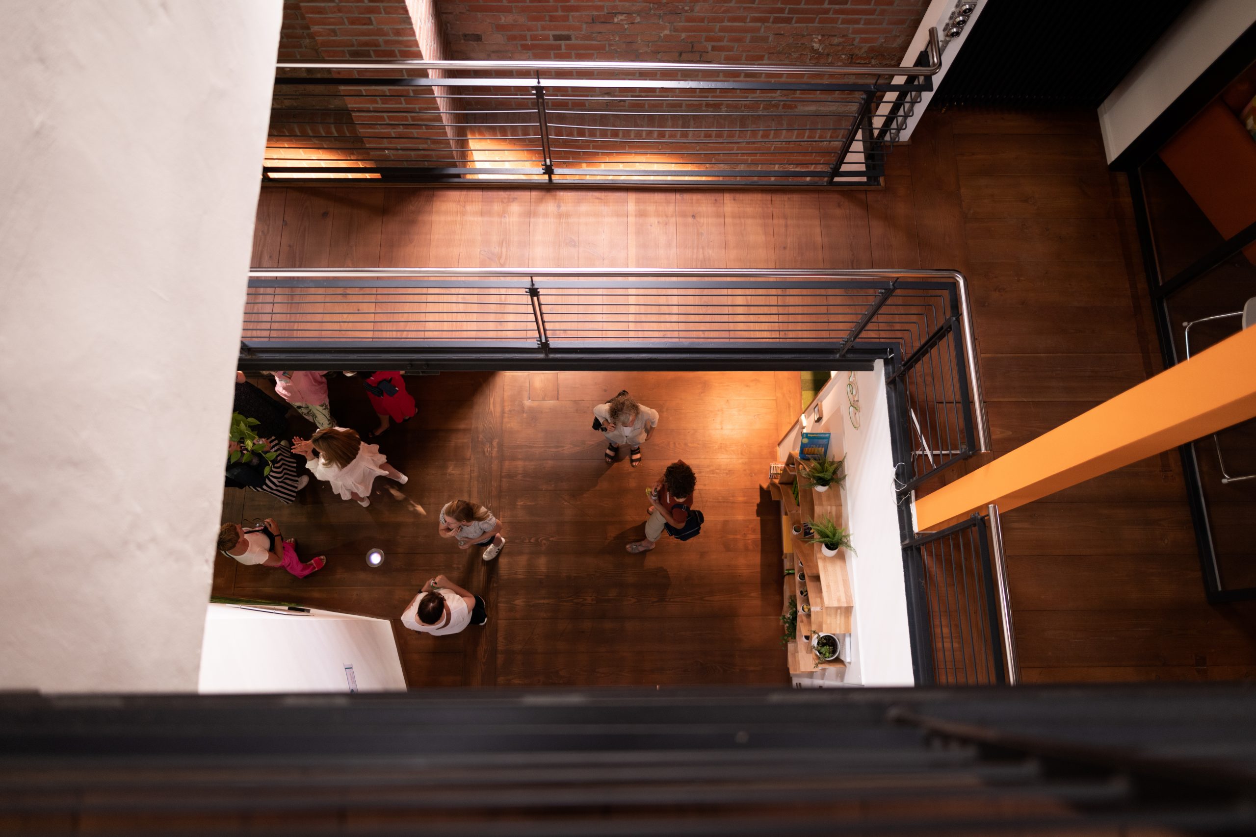 Top-down view of people socializing in a modern office space with wooden floors and metal railings.