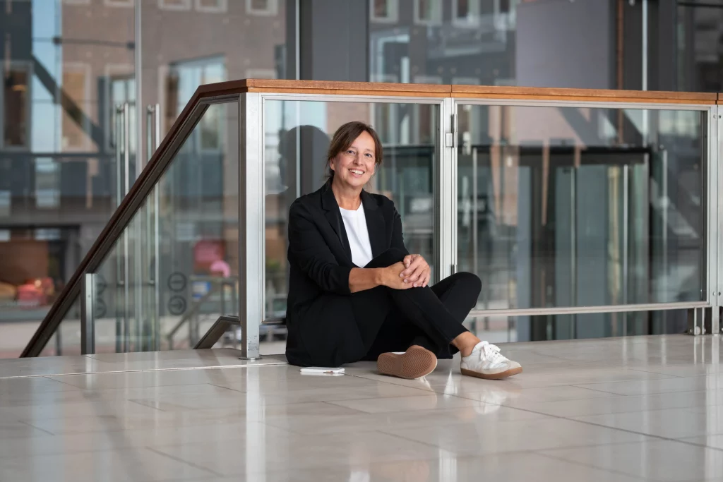Professionelles Businessfoto einer Frau im modernen Bürogebäude, sitzt entspannt auf dem Boden und lächelt freundlich.